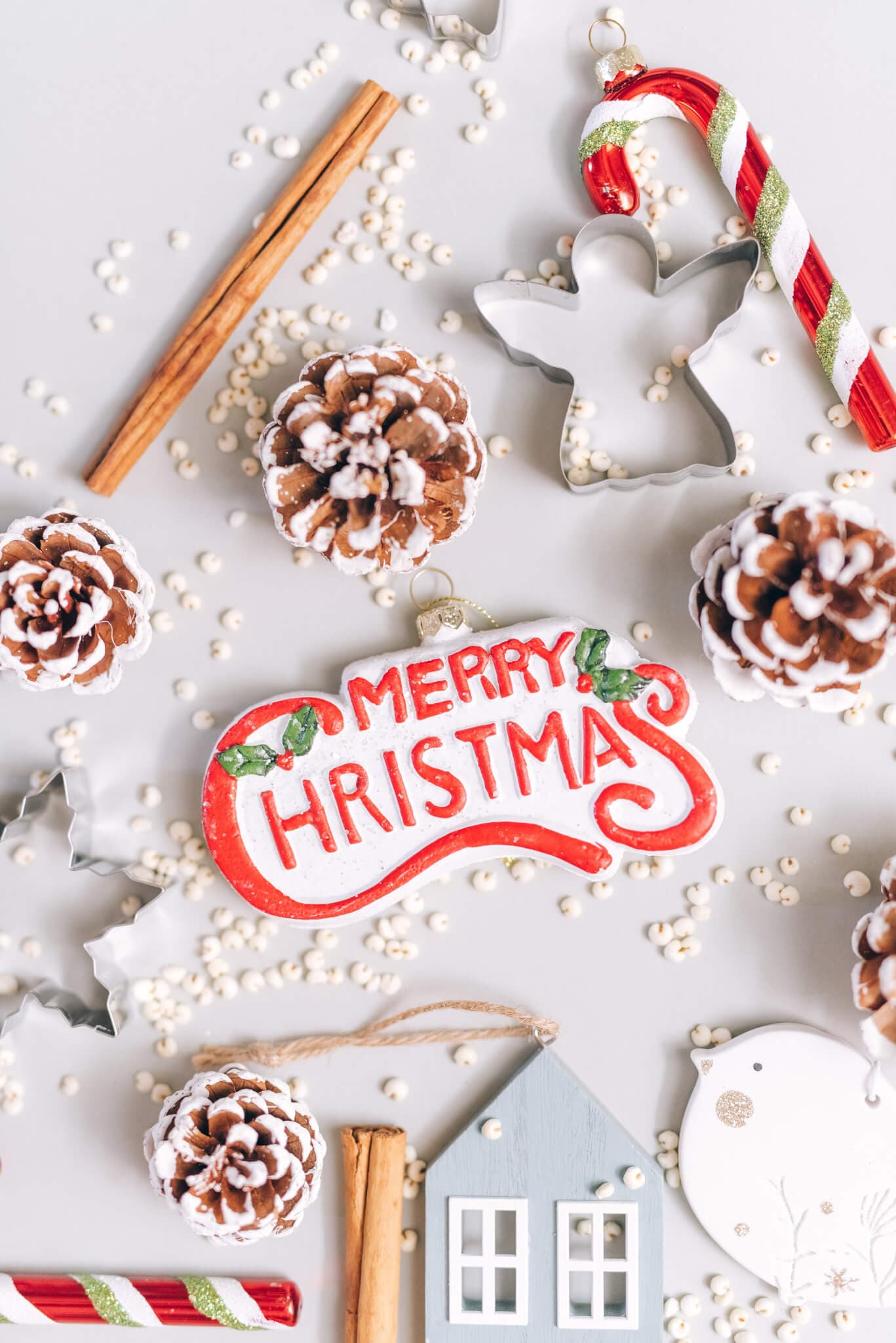 Christmas-themed flat lay with "Merry Christmas" ornament, pinecones, candy canes, cinnamon sticks, and cookie cutters. - Home Instead