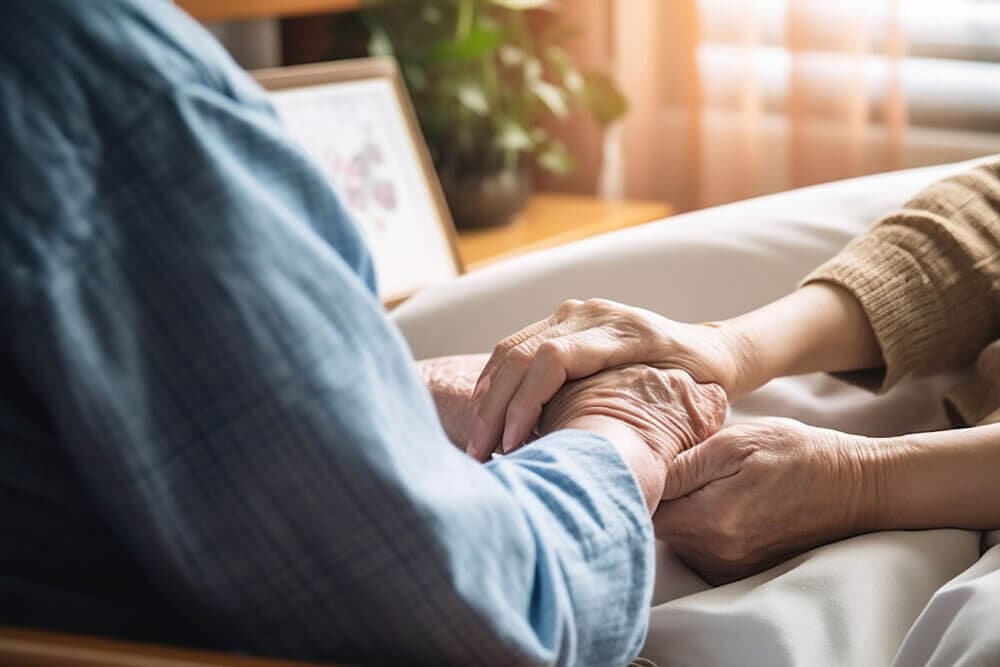 Two people holding hands in a comforting manner, one wearing a blue shirt and the other a tan sweater. - Home Instead