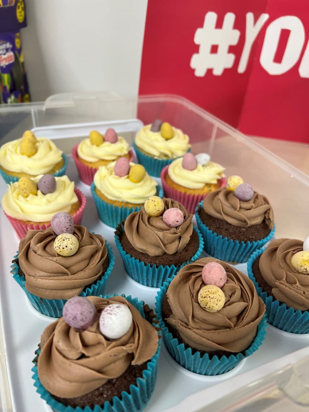 Chocolate and vanilla cupcakes with mini eggs on top, arranged in a plastic container. - Home Instead