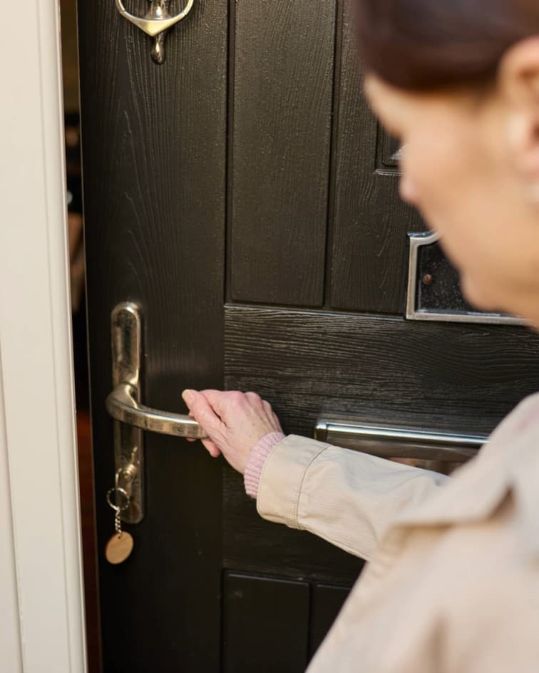 A person opening a black door while holding the silver door handle, keys hanging in the lock. - Home Instead
