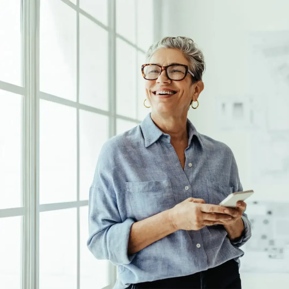 Older lady smiling and looking towards the camera while using her mobile phone