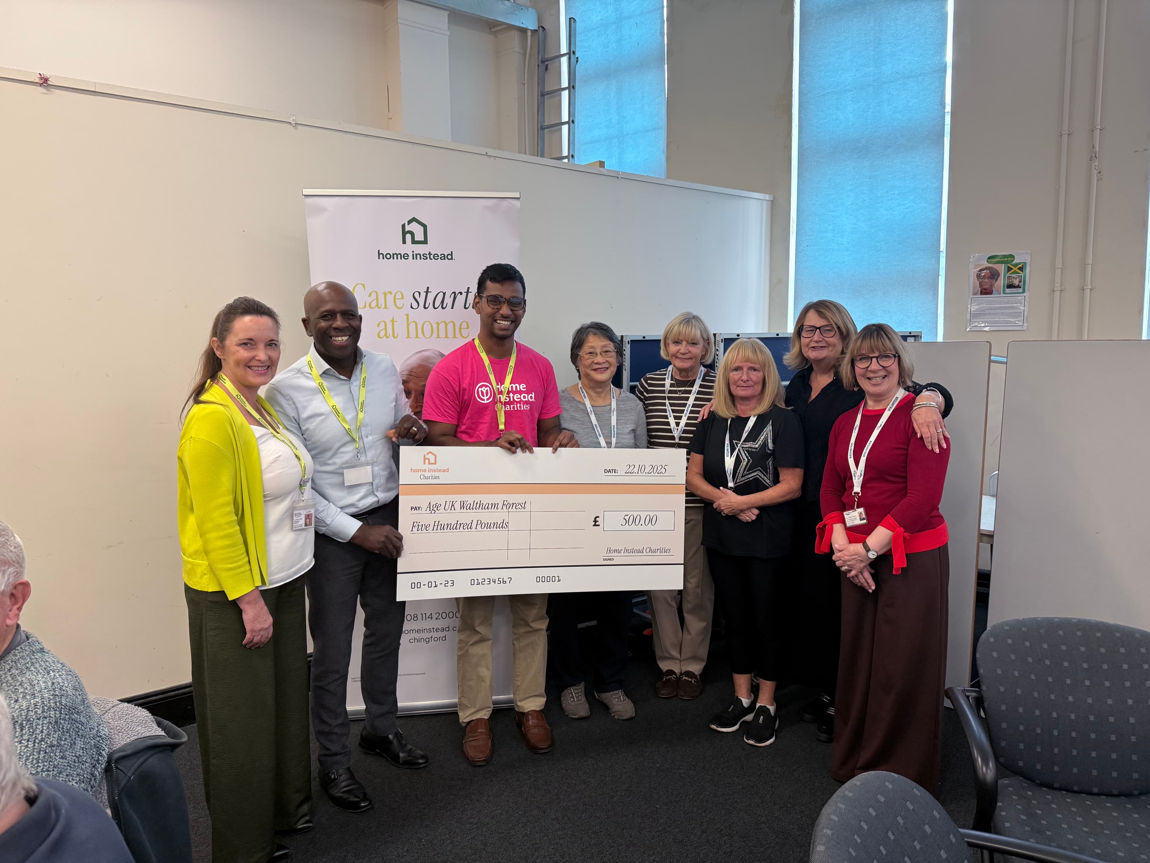 Nine people stand together smiling and holding a large $500 check at a community event. - Home Instead