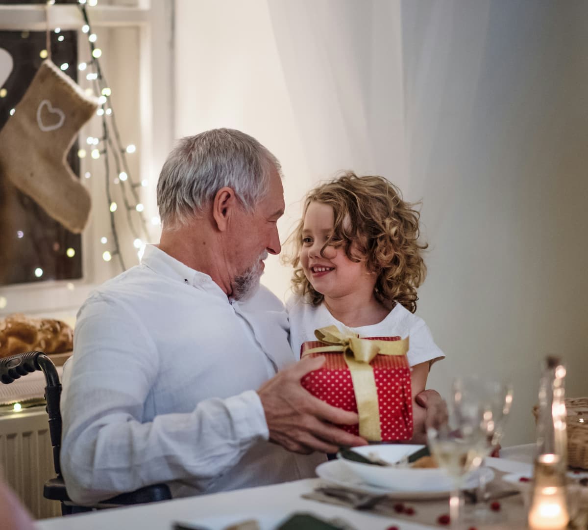 A girl with short curly hair happy and smiling while holding a giftt with an older male adult with grey hair while sitting on the dining table