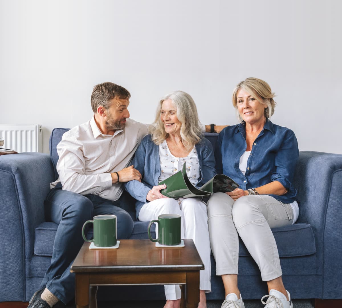 Three people sitting on a couch smiling while chatting together and having coffee