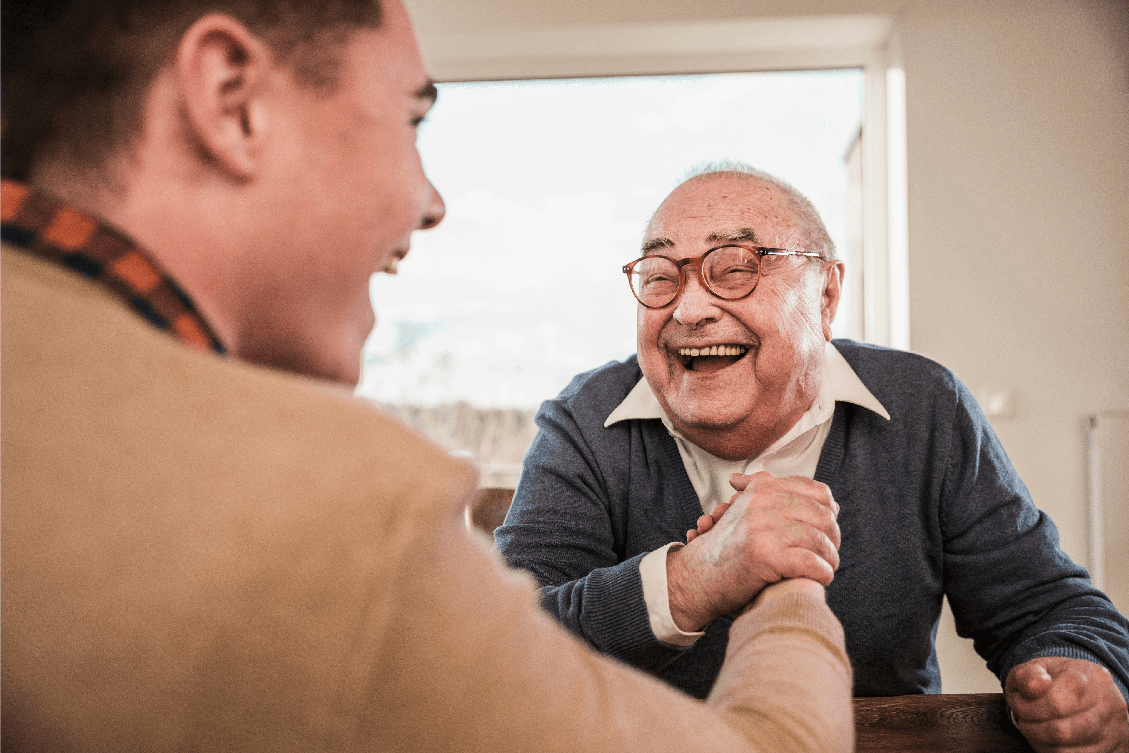 A young man and an elderly man laughing whilst arm wrestling. - Home Instead