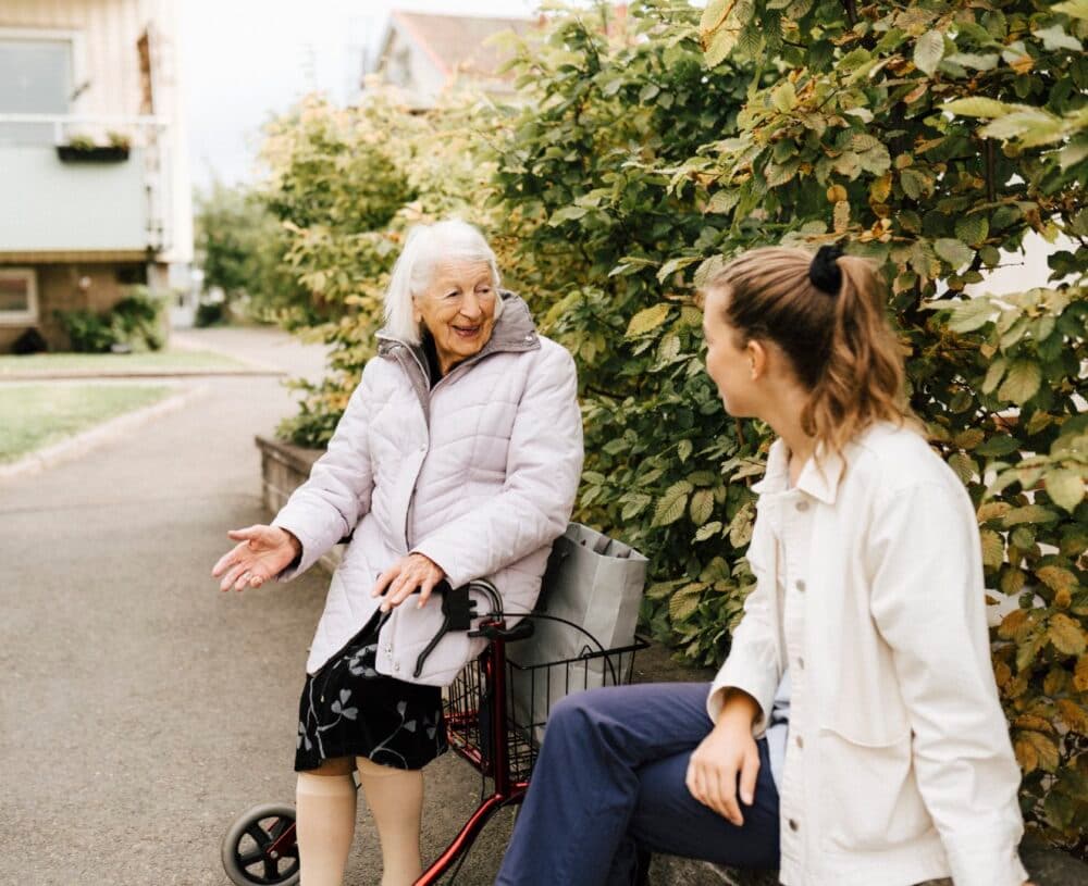 Smiling senior woman talking with female nurse at front yard