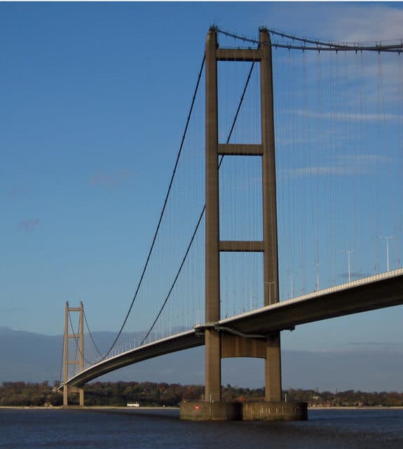 A large suspension bridge spanning a body of water under a clear blue sky. - Home Instead