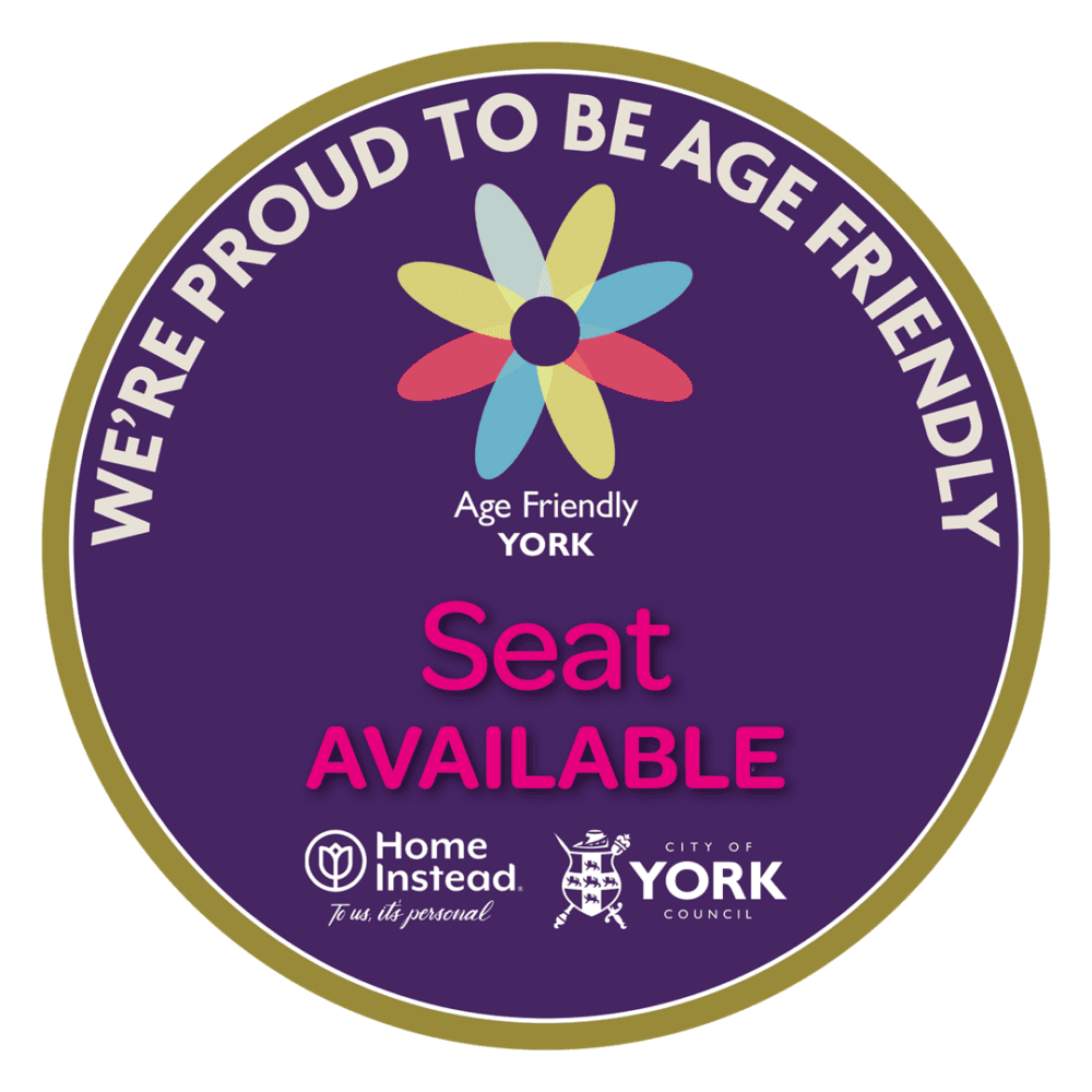 A round sign with "We're Proud to Be Age Friendly" and "Seat Available" text, featuring logos of Home Instead and York Council. - Home Instead