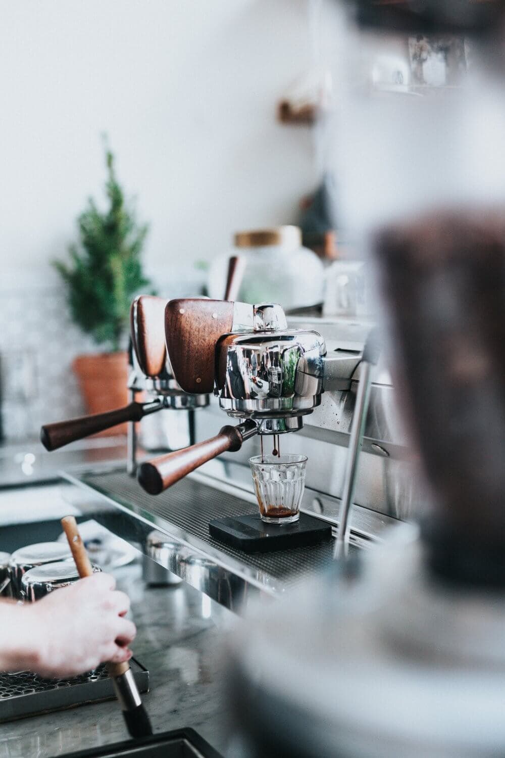 Close-up of a professional espresso machine making coffee with a barista's hand in the foreground. - Home Instead