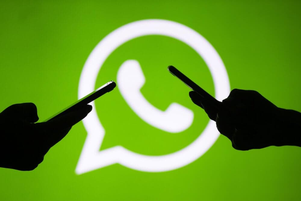 Silhouettes of two people holding smartphones against a WhatsApp logo background. - Home Instead