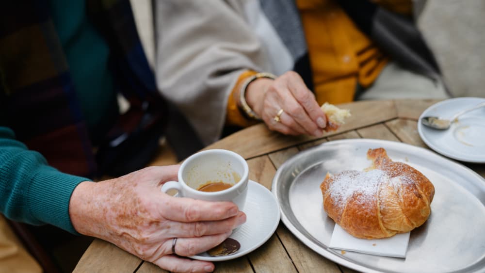 An elderly person enjoying a coffee and croissant at a cafe in Winchester - Home Instead Central Hampshire