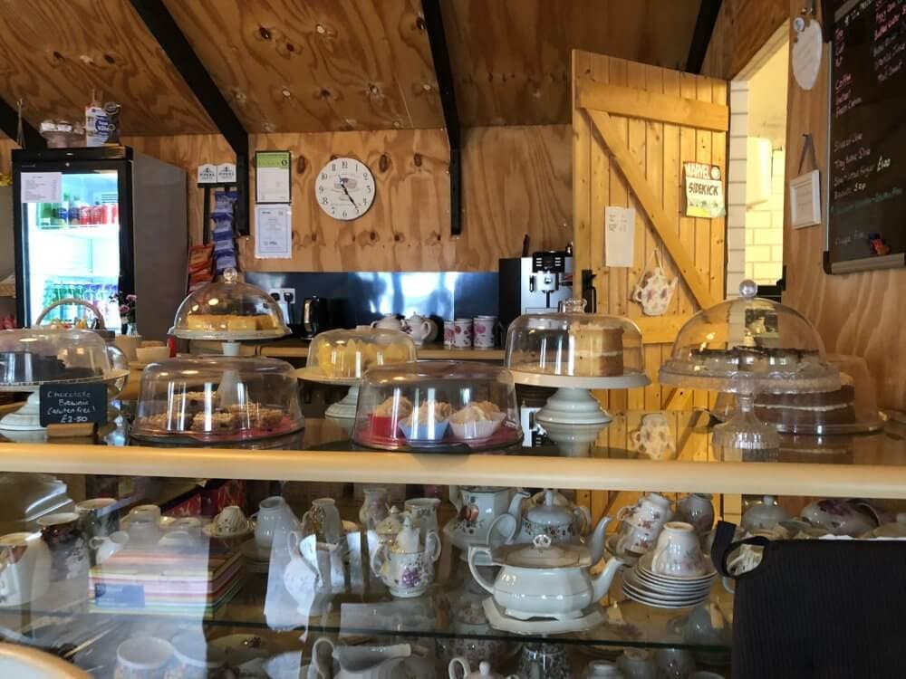 Interior of a cozy cafe with cakes on display under glass domes, shelves with teapots, and a rustic wooden background. - Home Instead