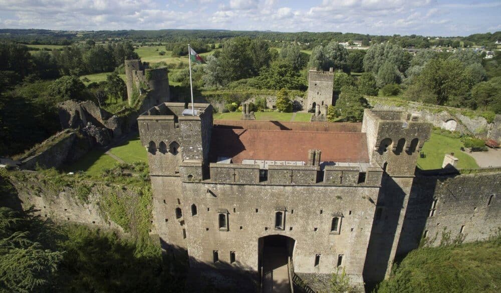 Aerial view of a historic stone castle with towers, surrounded by lush green landscape on a sunny day. - Home Instead