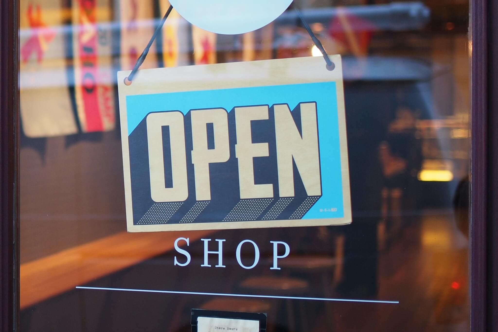 Shop window with a blue and yellow "Open" sign hanging, indicating the store is open for business. - Home Instead