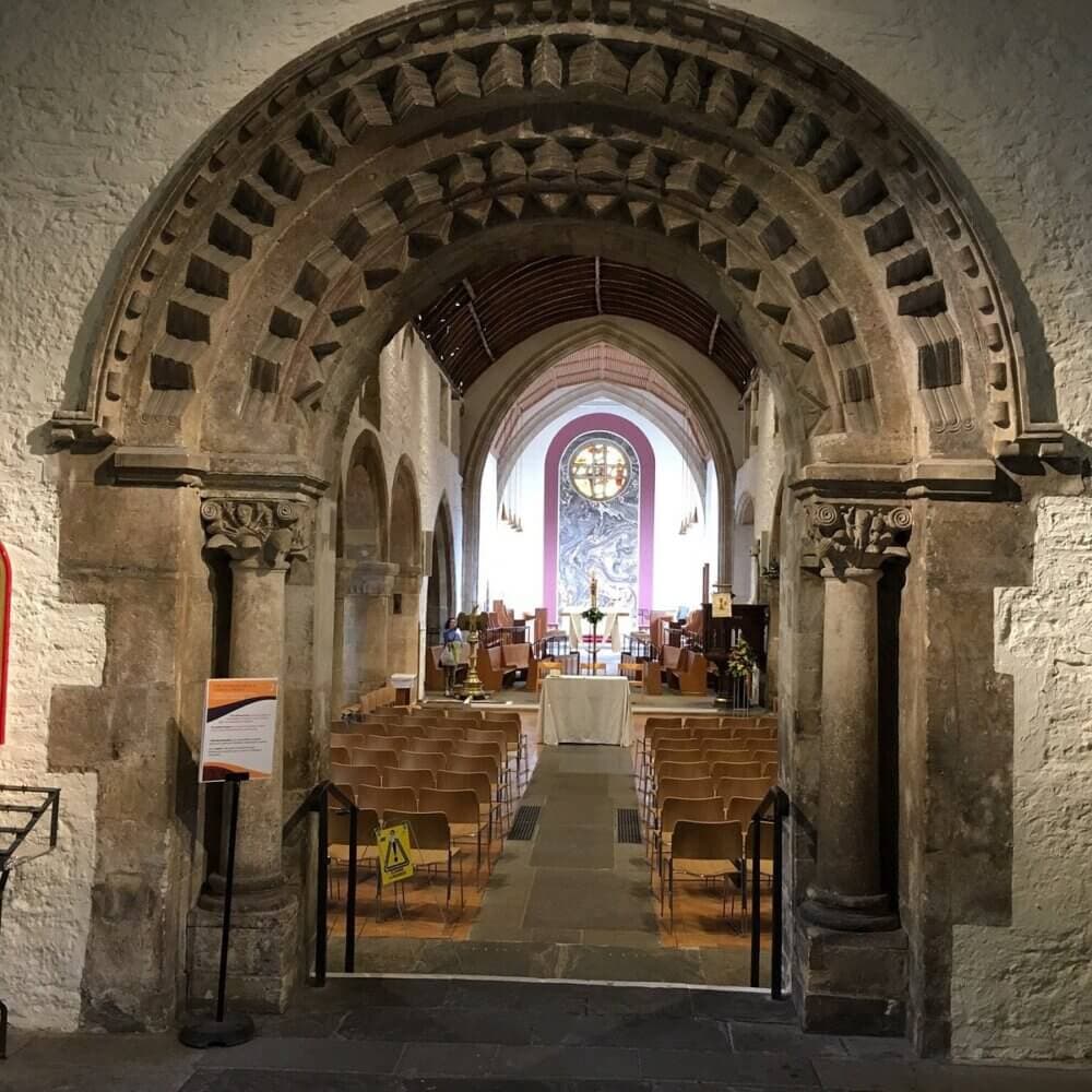 View of a church interior with arched stone entrance, rows of chairs, and altar in the distance. - Home Instead