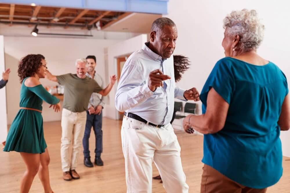 A group of people of various ages dance together in a brightly lit room. - Home Instead