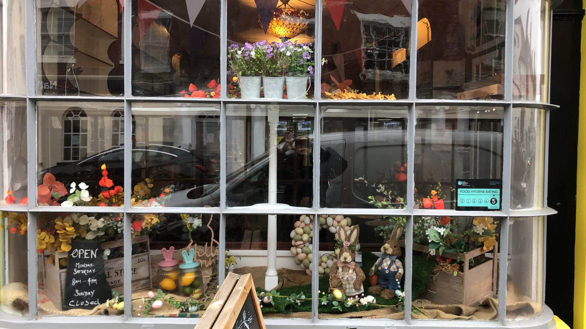 A store window display with flowers, Easter decorations, and a sign indicating the store's open and closing times. - Home Instead