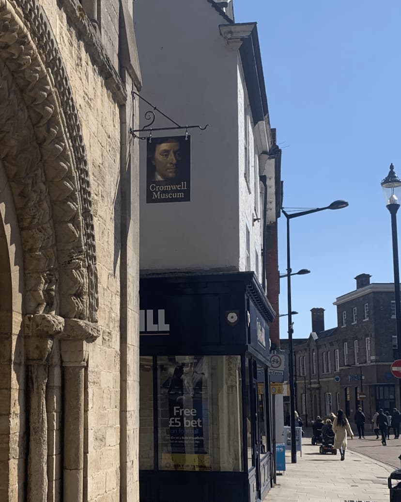 Street view with Cromwell Museum sign on building, blue store below, and people walking in the background on a sunny day. - Home Instead