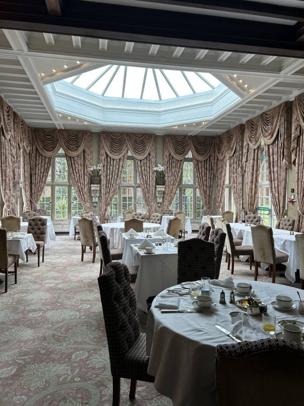 Home Instead Basingstoke picture of the elegant dining room with round tables, chandeliers, large windows and a glass ceiling at Tilney Hall, near Basingstoke