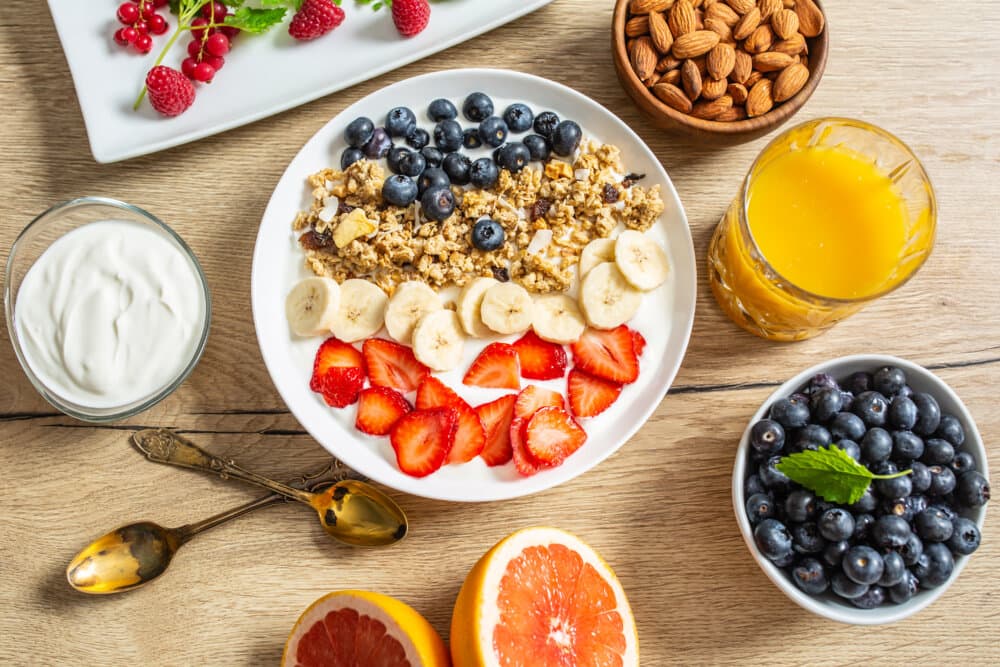 A breakfast spread with yogurt, granola, berries, banana, sliced strawberries, almonds, orange juice, and grapefruit. - Home Instead