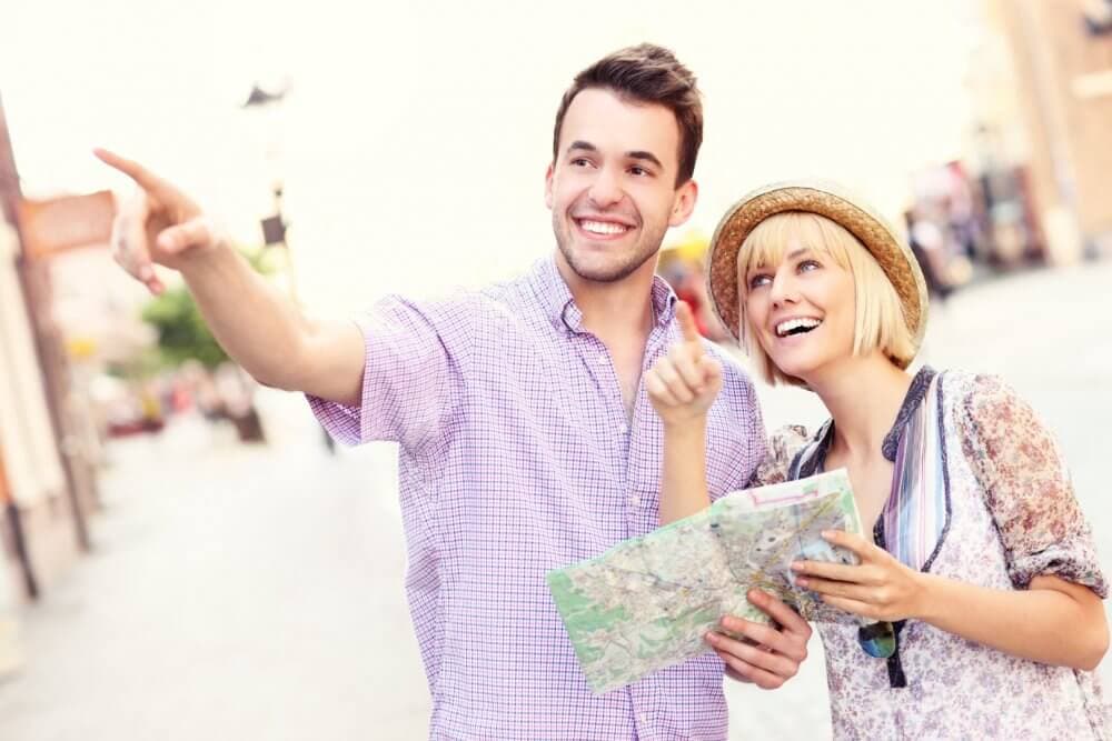 A smiling man and woman with a map enjoy sightseeing, pointing in the direction they plan to go. - Home Instead