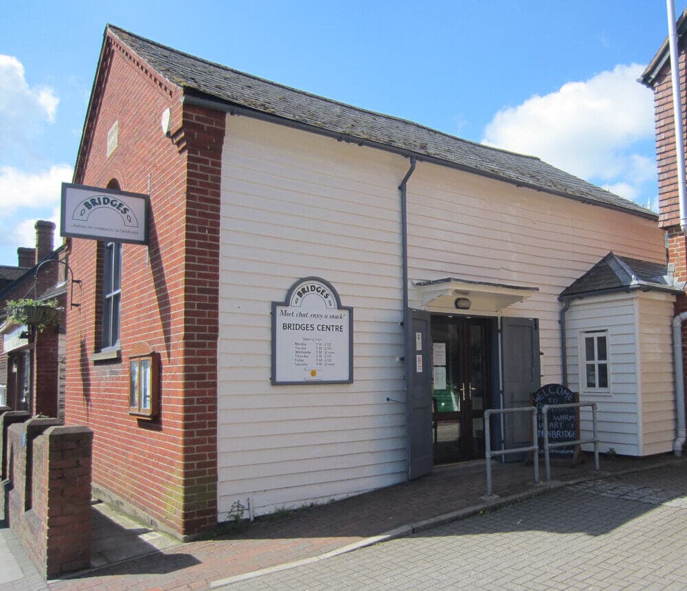 Exterior of Bridges Centre, a red-brick building with white siding, a sign above the entrance, and an information board. - Home Instead