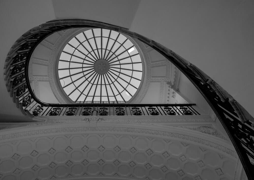 Black and white spiral staircase with ornate railing leading up to a domed skylight with geometric patterns. - Home Instead