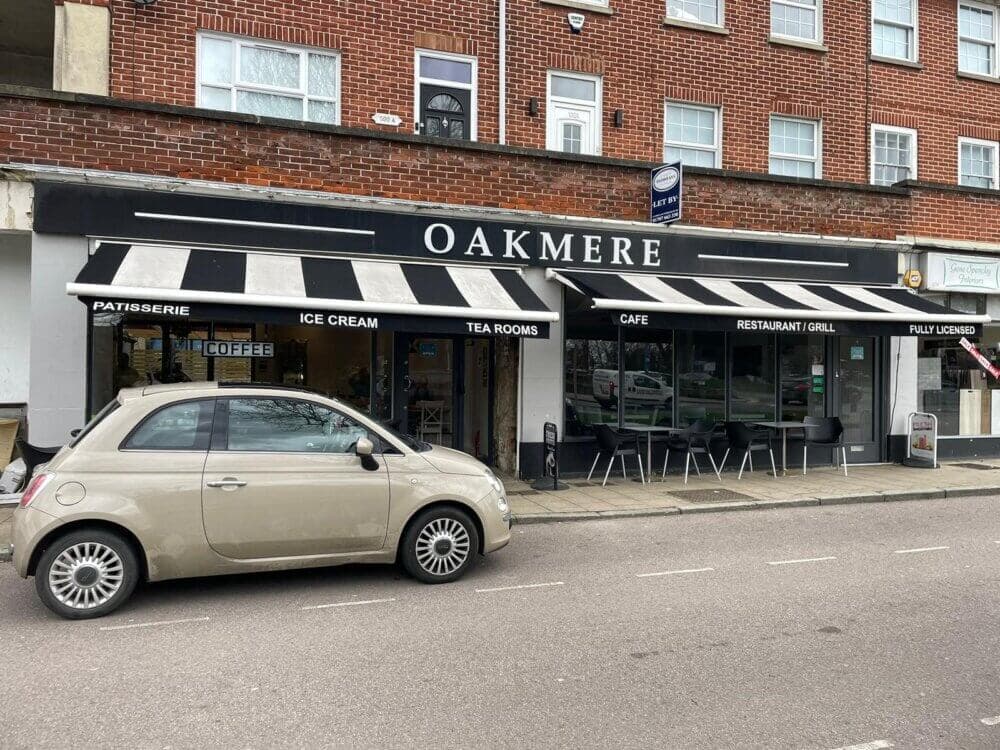 A storefront with a black and white awning labeled "OAKMERE." A small beige car is parked in front. - Home Instead