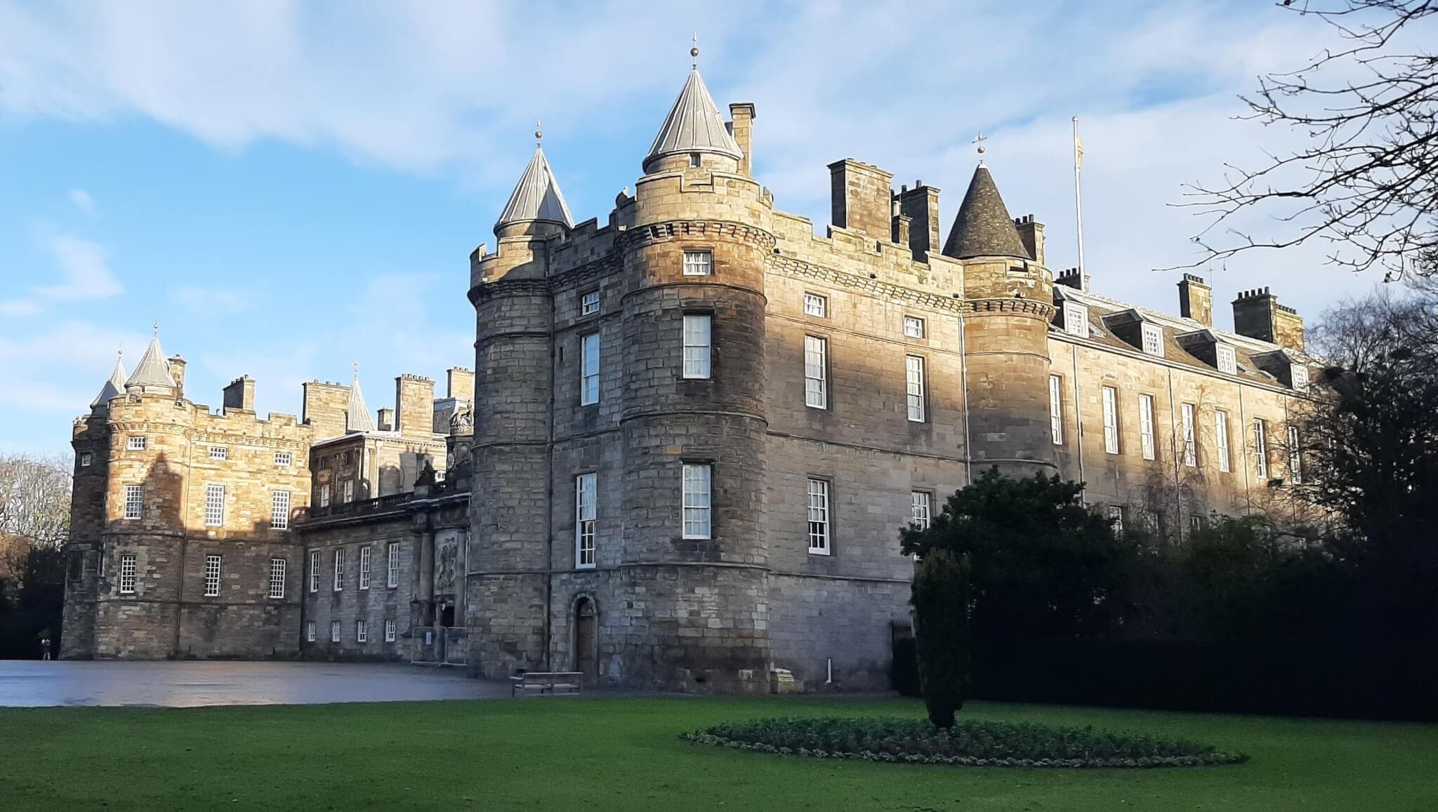A grand, historic stone castle with turrets, set against a blue sky and surrounded by lush greenery. - Home Instead