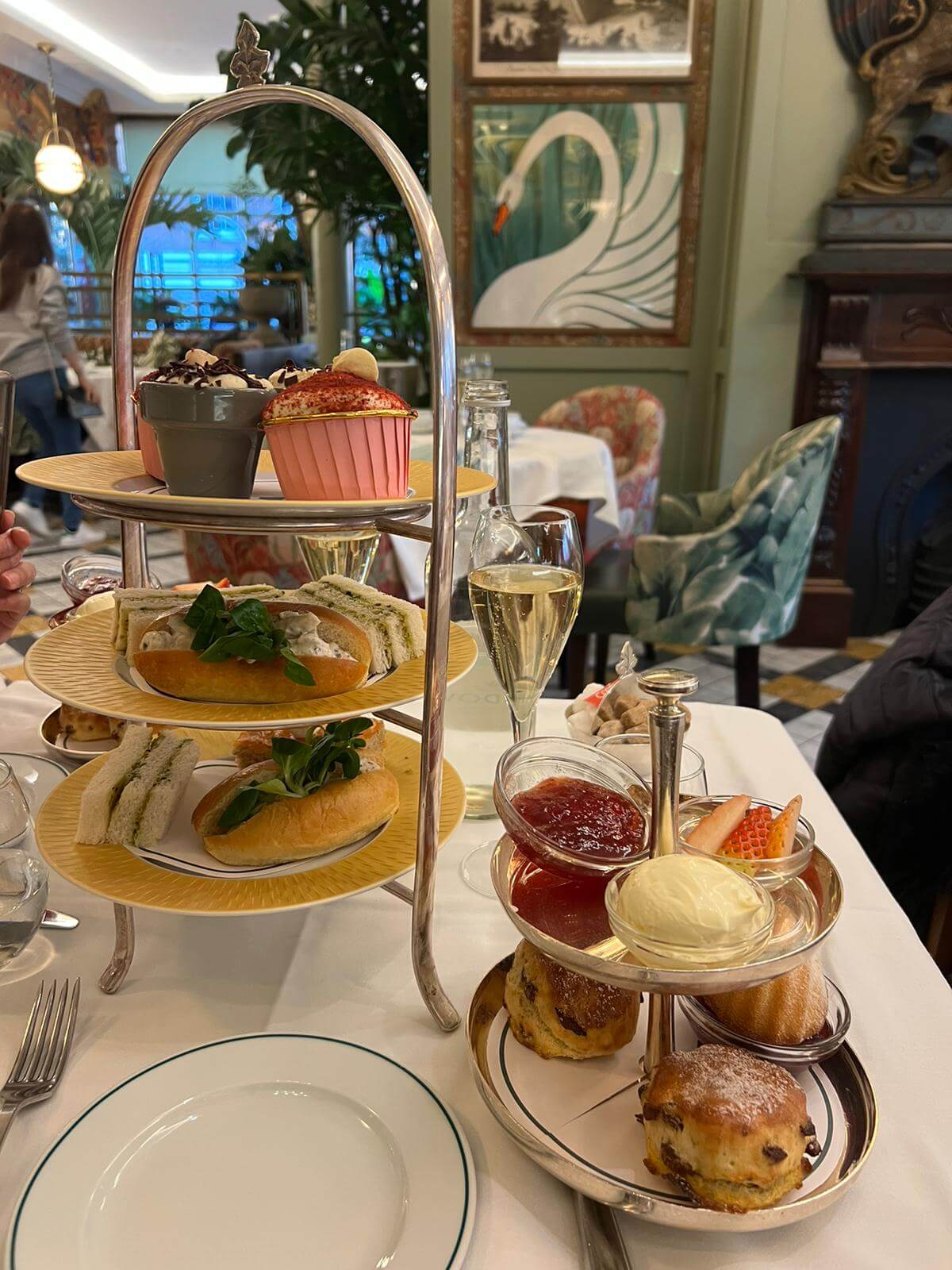 An elegant afternoon tea setup with sandwiches, pastries, scones, and preserves, served with champagne in a cozy setting. - Home Instead