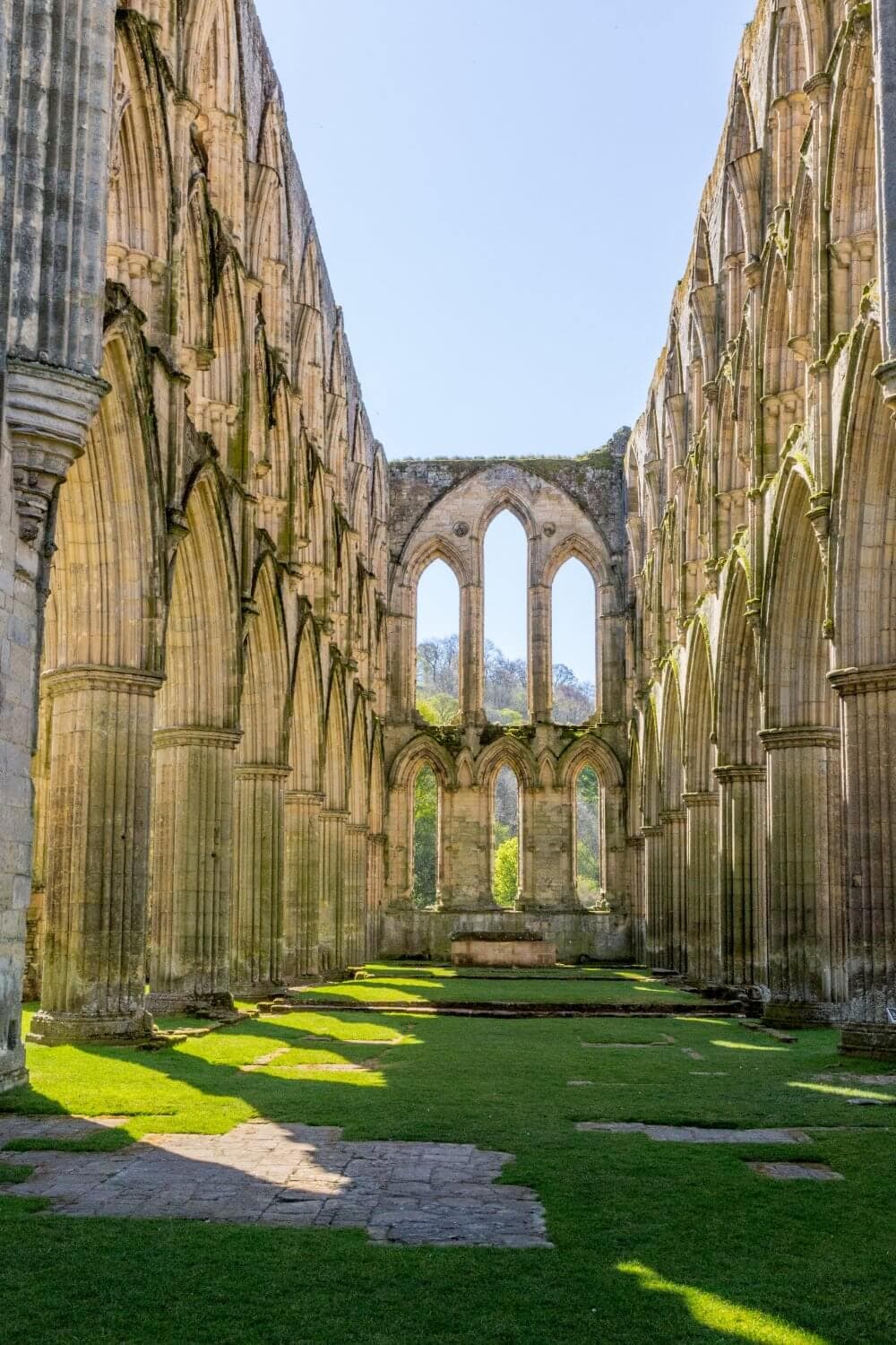 Tall stone arches and columns of an ancient cathedral ruin with green grass underfoot and sunlight streaming through. - Home Instead