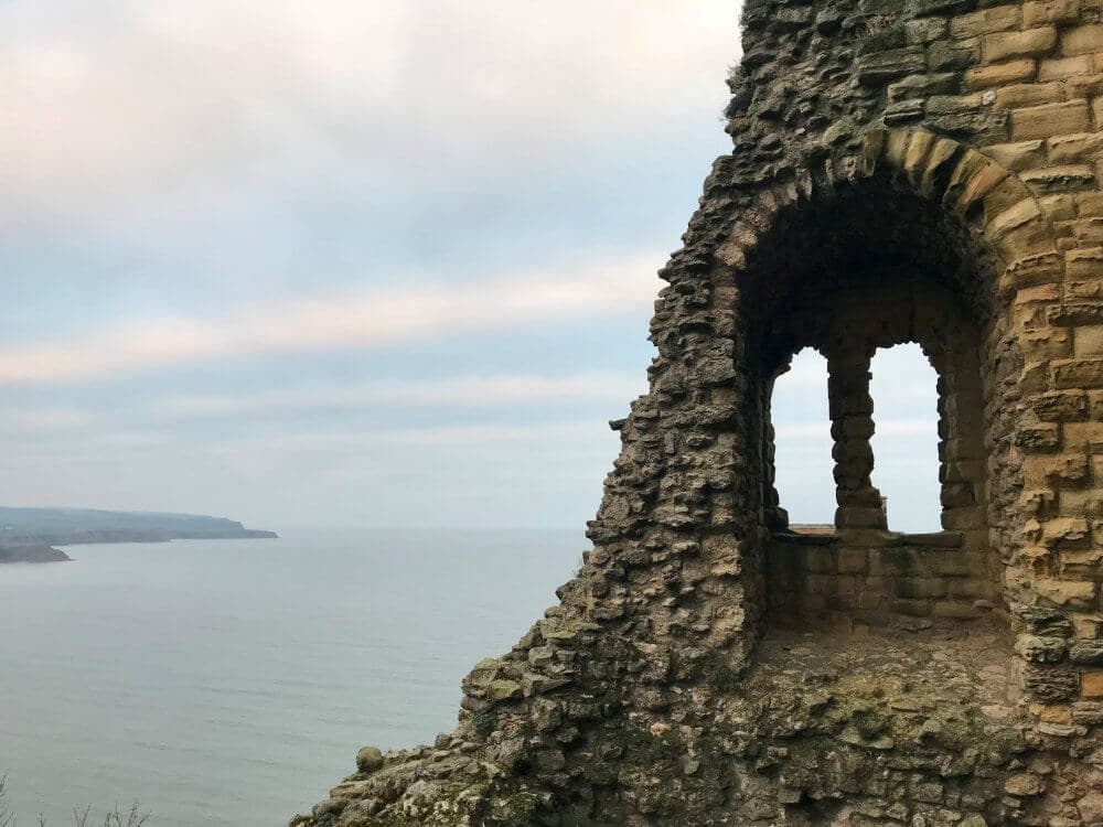 A crumbling stone window in an ancient castle overlooks a calm sea under a cloudy sky. - Home Instead
