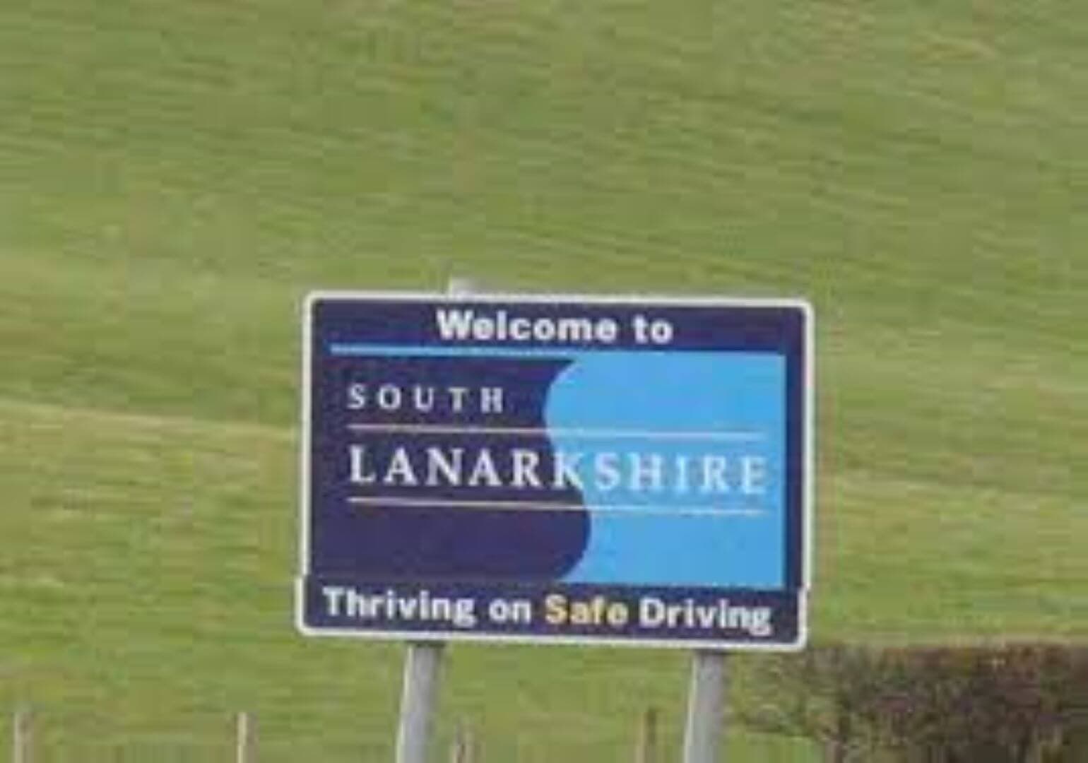 Road sign reading "Welcome to South Lanarkshire" with subtext "Thriving on Safe Driving" in a grassy landscape. - Home Instead