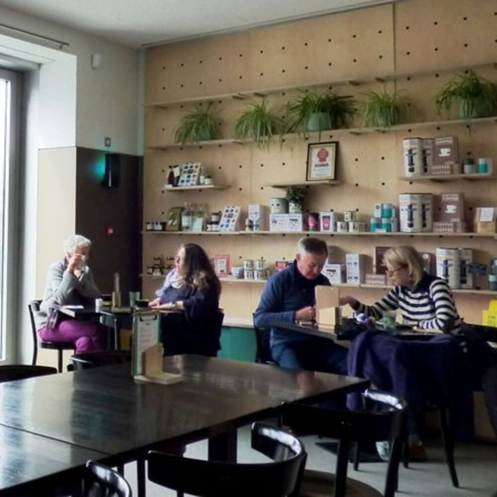 People dining and conversing at a cafe with shelves featuring plants and various items in the background. - Home Instead