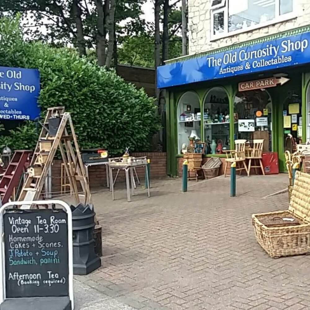 Antique shop with vintage decor, outdoor furniture, and a sign promoting a tea room offering cakes, scones, and sandwiches. - Home Instead