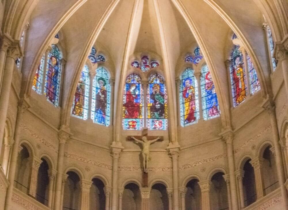 Interior of a cathedral with a vaulted ceiling, stained glass windows, and a crucifix in the center. - Home Instead