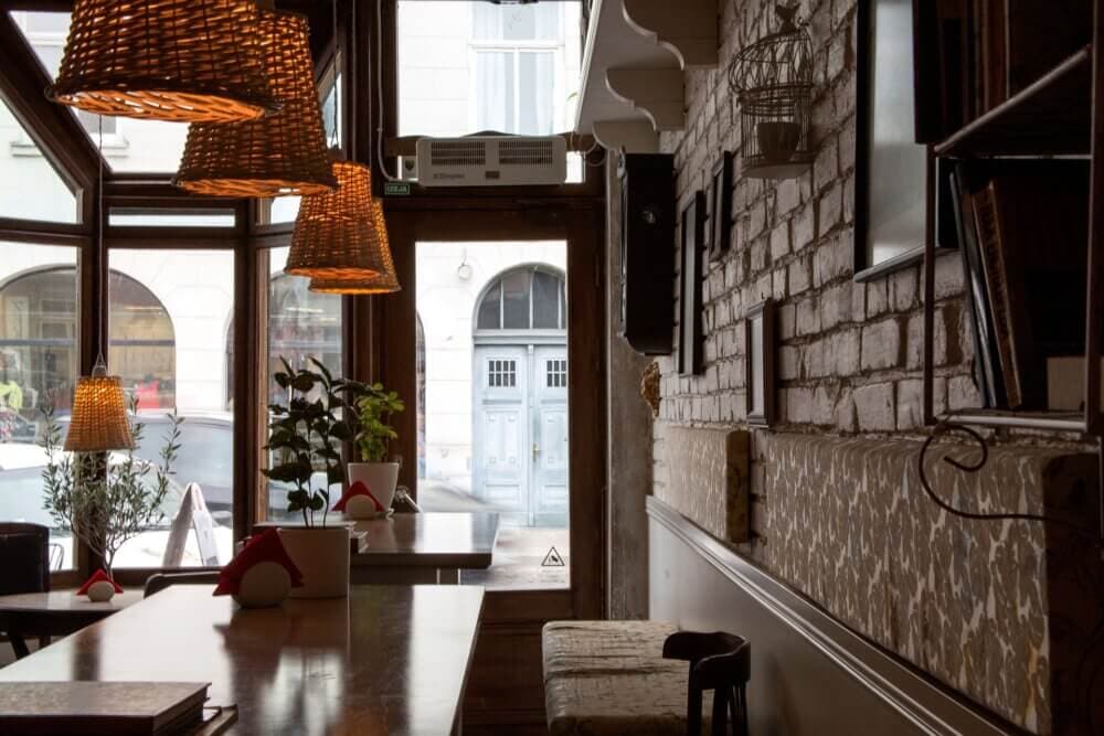 Cozy café interior with wicker lamps, wooden tables, brick walls, and a view of the door leading outside. - Home Instead