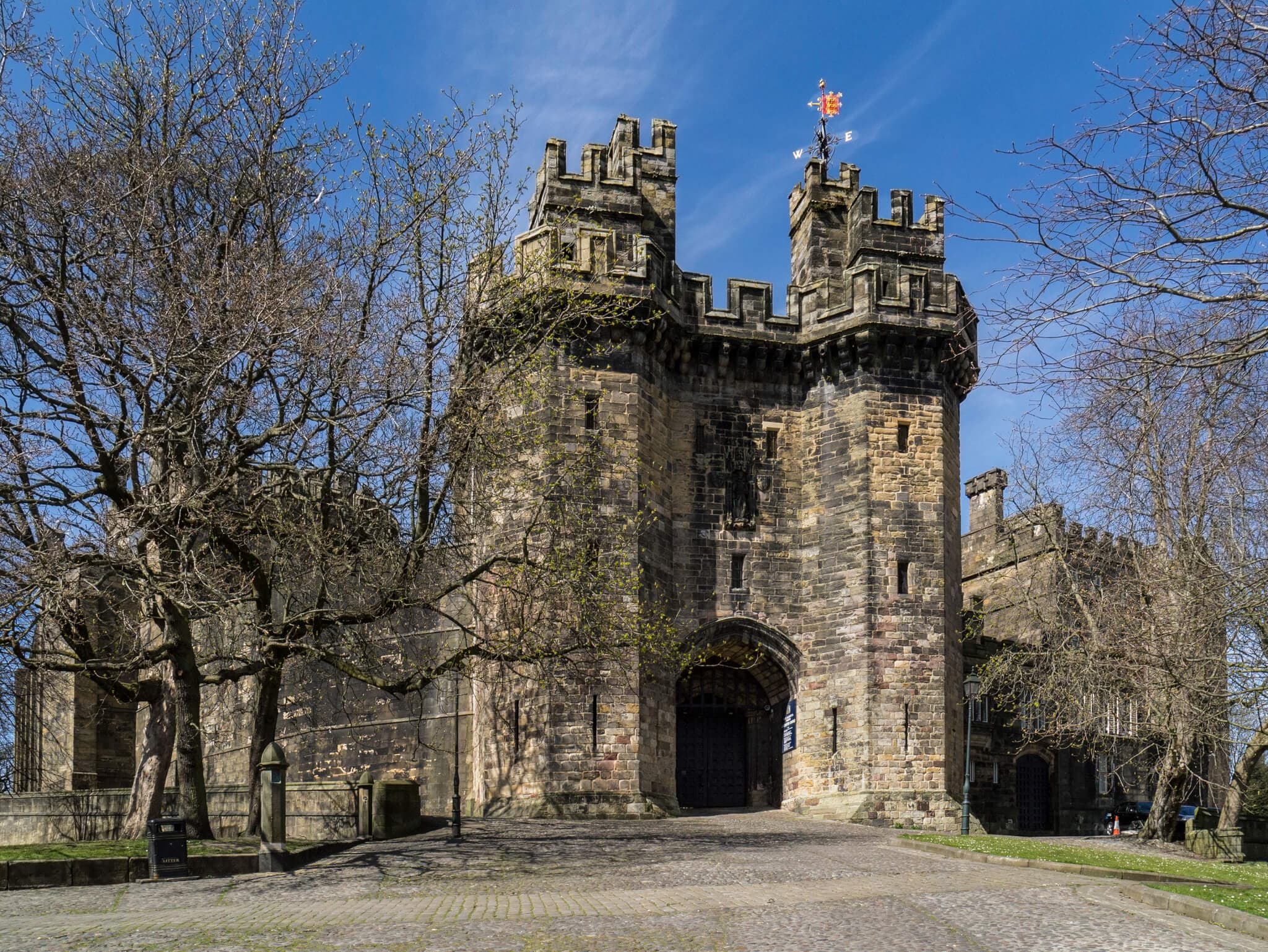A stone medieval castle with a central arched gate, surrounded by trees, under a clear blue sky. - Home Instead