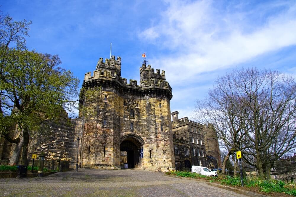 Historic stone castle with prominent entrance gate, surrounded by trees, under a blue sky with white clouds. - Home Instead
