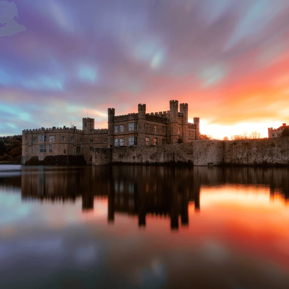 A grand castle with towers and turrets reflected in the water under a vibrant, colorful sunset sky. - Home Instead