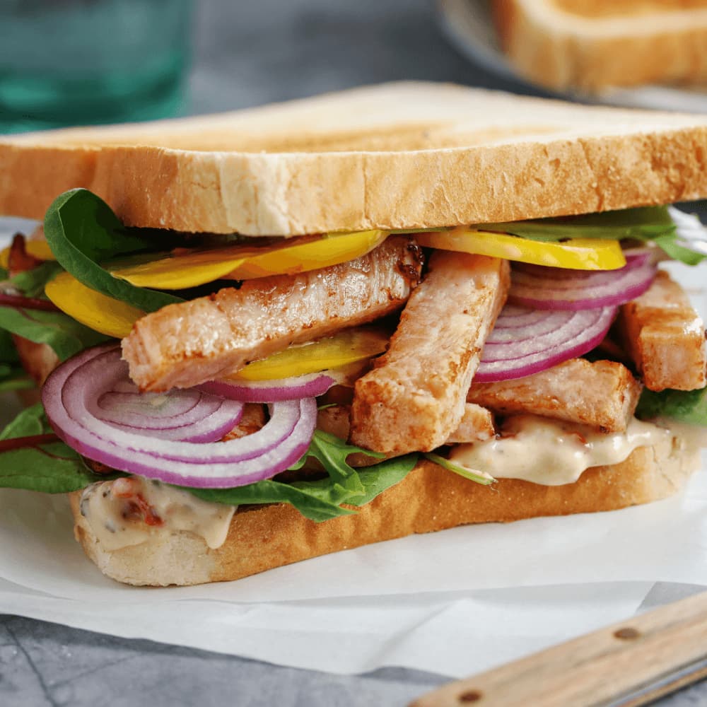 A sandwich with grilled chicken, spinach, yellow bell peppers, red onions, and sauce on white bread. - Home Instead