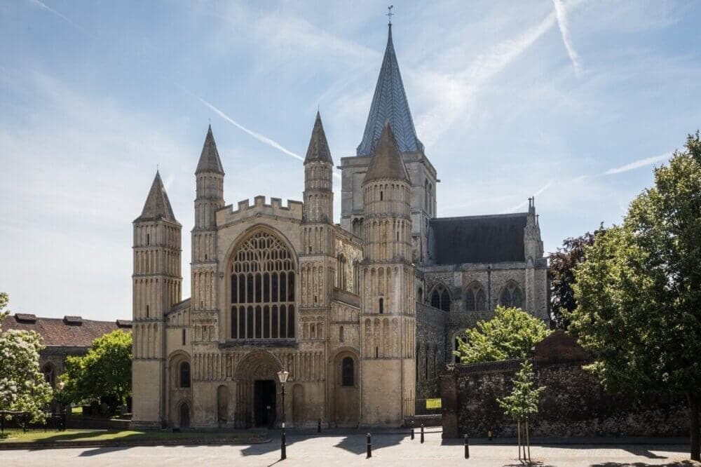 A large stone cathedral with tall spires and a central entrance, set against a clear blue sky and surrounding trees. - Home Instead