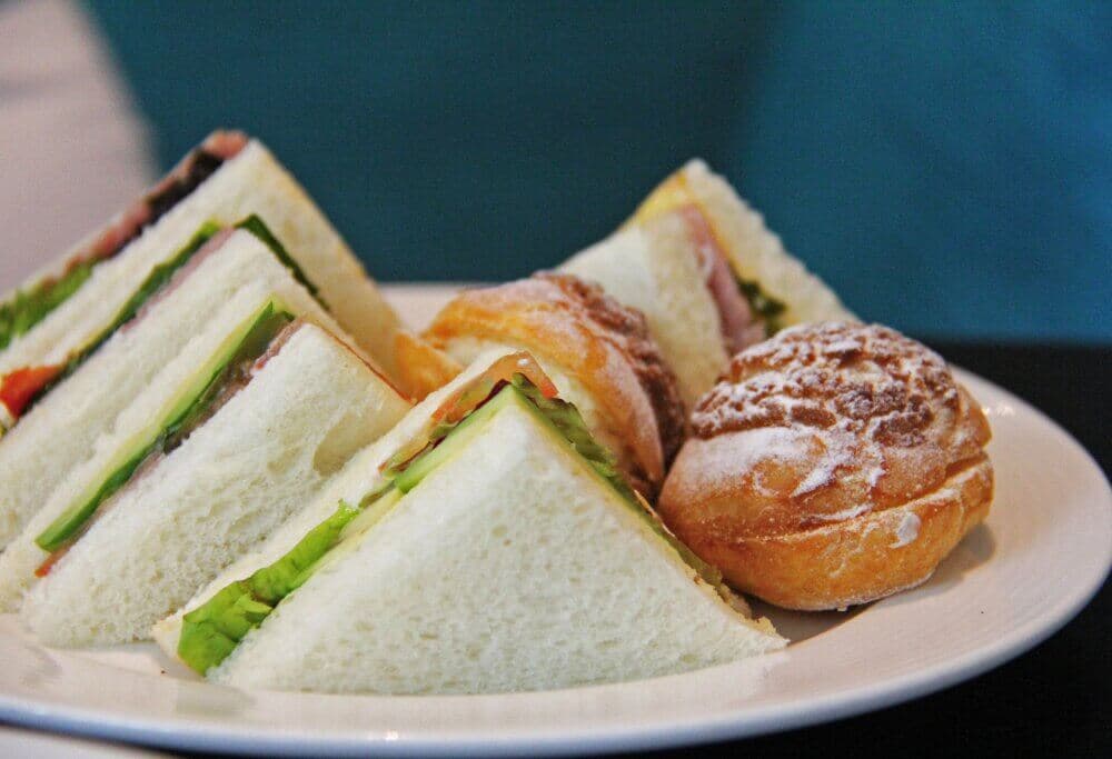 A plate with sandwich triangles filled with vegetables and ham alongside a powdered cream puff pastry. - Home Instead