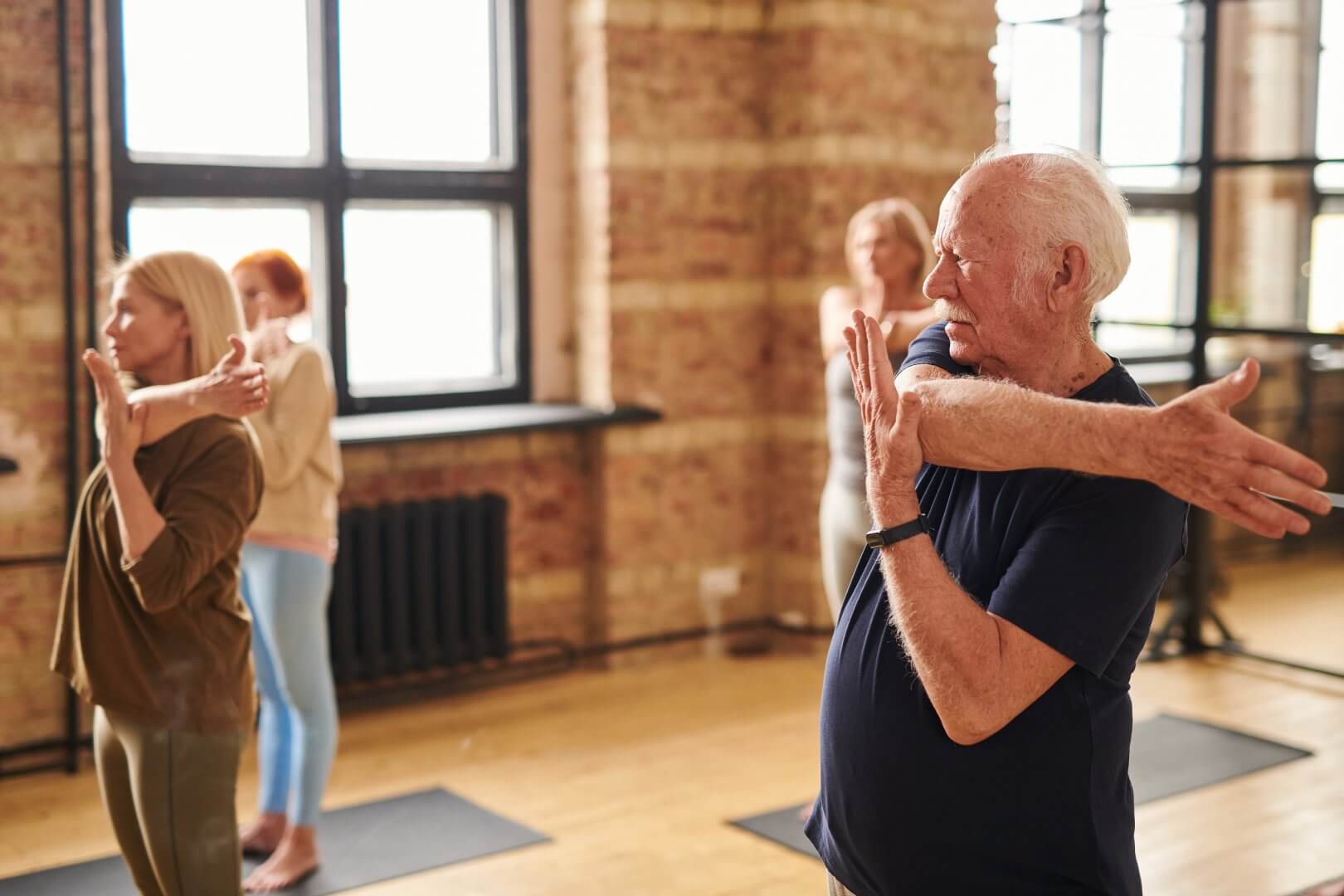 People in a fitness class stretch their arms in a well-lit studio with brick walls and large windows. - Home Instead