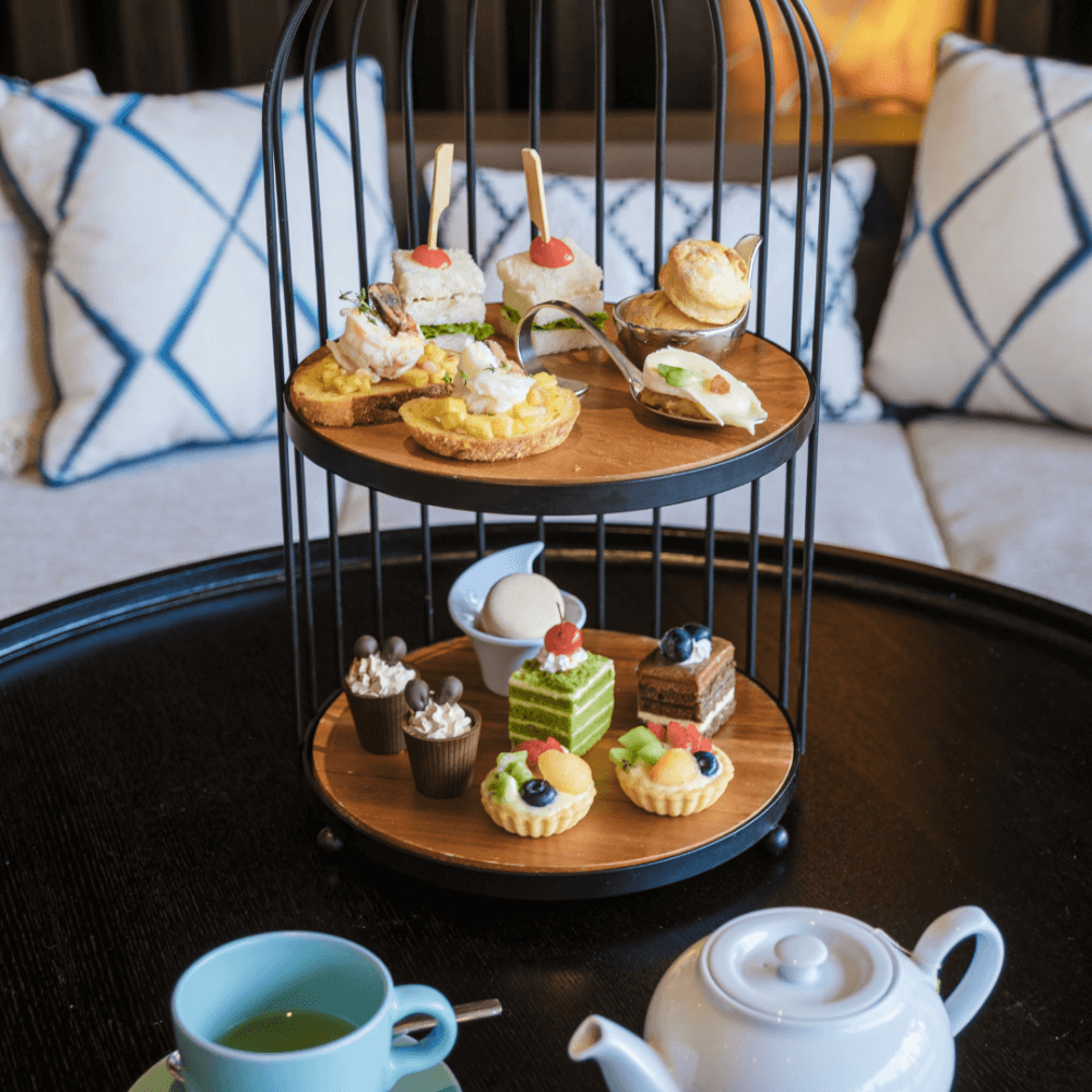 Two-tiered tray with assorted desserts and appetizers on a black table, teal cup and white teapot beside it. - Home Instead