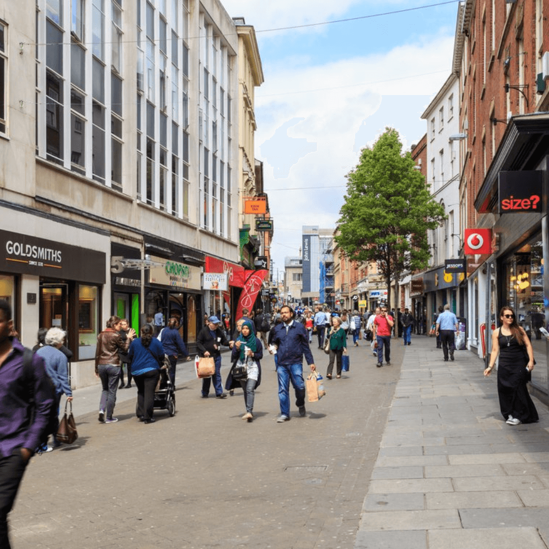 Busy commercial street scene with people walking by shops including Goldsmiths, Game, and Size? on a sunny day. - Home Instead