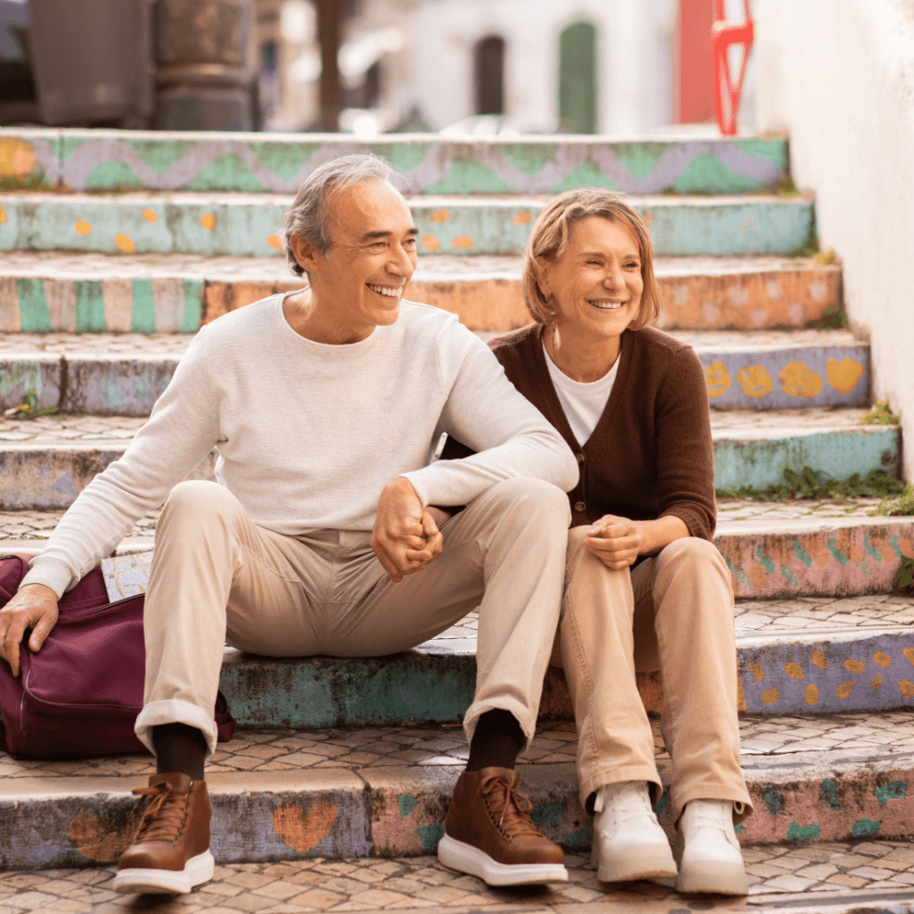 Happy elderly couple sitting on colorful steps, smiling and enjoying a sunny day outdoors. - Home Instead