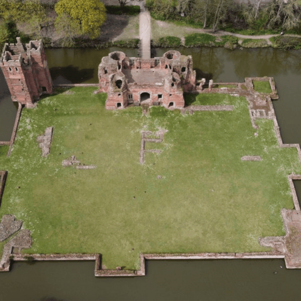 Aerial view of a medieval red brick castle ruin surrounded by a moat with lush greenery in the background. - Home Instead