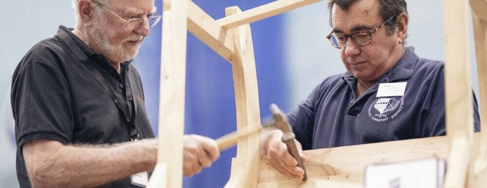 Two men work together with hammers to construct a wooden frame. - Home Instead