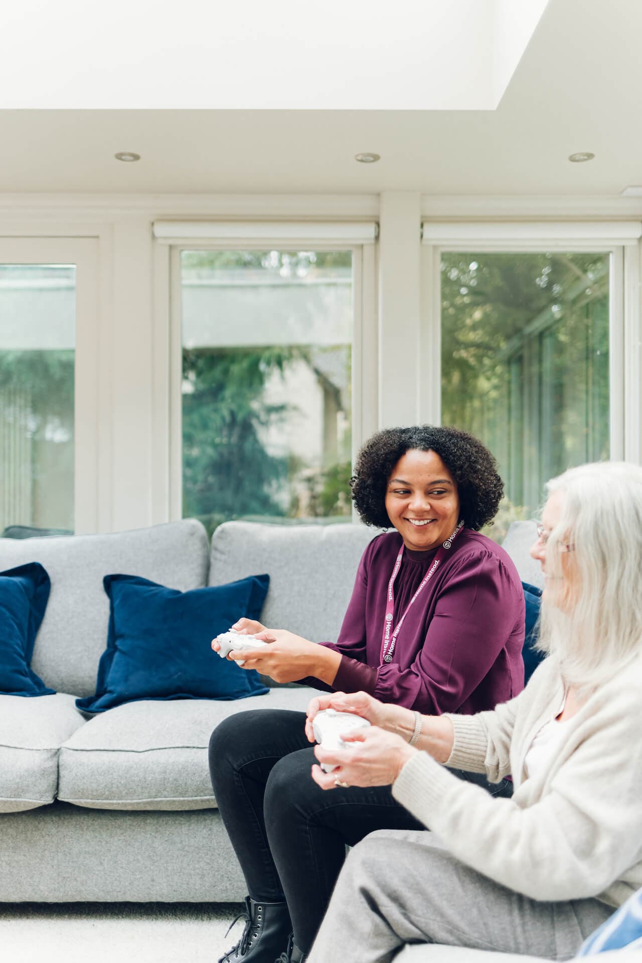Care Professional and client sitting on a couch, smiling and playing video games in a bright living room. - Home Instead Bournemouth & Christchurch